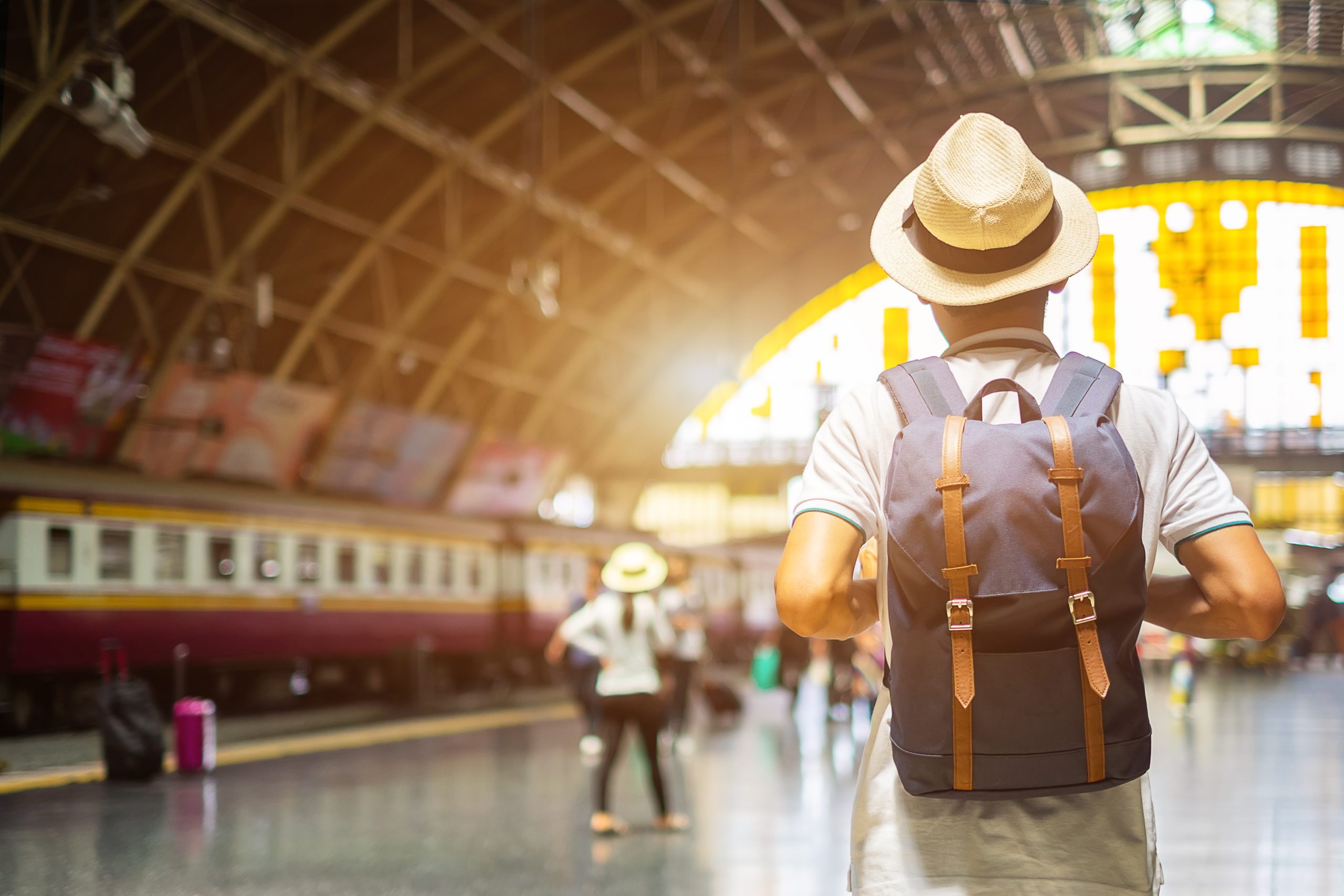 Young man traveler with backpack waiting for train, Asian backpacker with hat standing on railway platform at Bangkok train station. Holiday, journey, trip and summer Travel concept